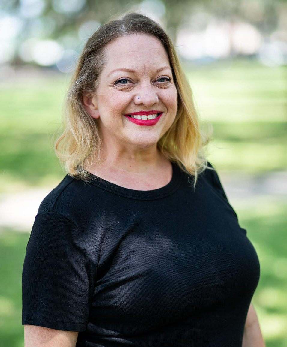 Professional headshot of smiling blonde woman in black top outdoors