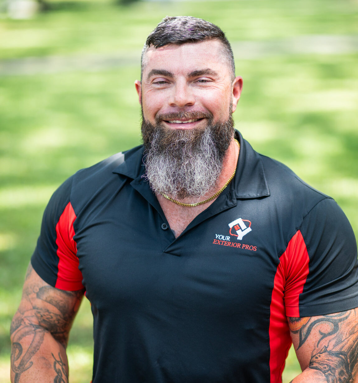 Smiling bearded man in Your Exterior Pros polo shirt with tattoos outdoors
