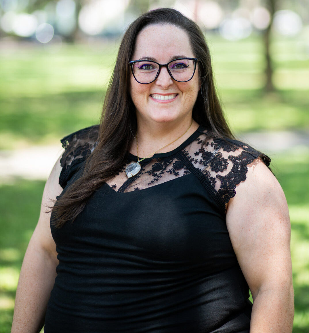 Smiling woman with glasses in black lace dress posing outdoors in natural setting